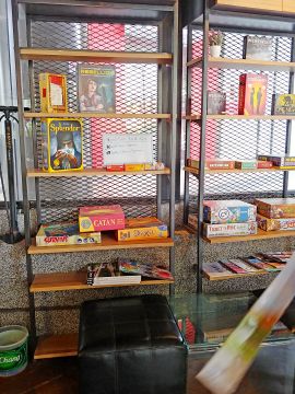 Shelves displaying board games like Catan and Splendor at Neolution Esport Store Board Game Cafe in Bangkok.