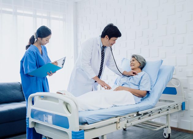 Asian Elderly Female Patient Dressed Light Blue Bed Male Doctor White Suit Uses Stethoscope Listen Heartbeat Checkup while Assistant Record Symptoms Follow Up