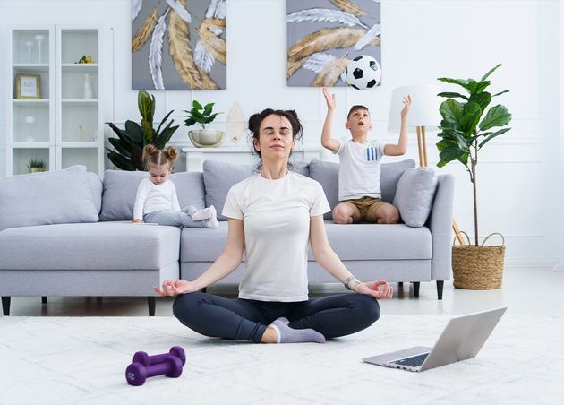 Young Mom Meditating Lotus Yoga Position while Her Children Playing Home