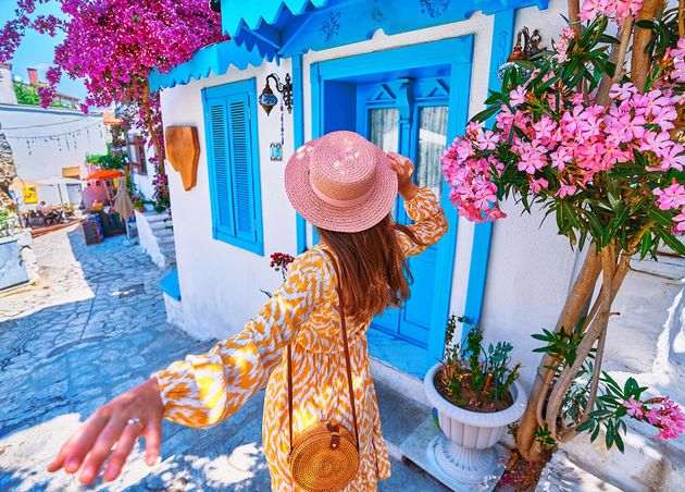 Follow Me Concept Girl Traveler Wearing Dress Hat Walks Beautiful Colorful Flower Street with White Houses Blue Doors European City