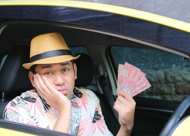 Asian Man Showing Sad Expression while Holding Money from inside His Car