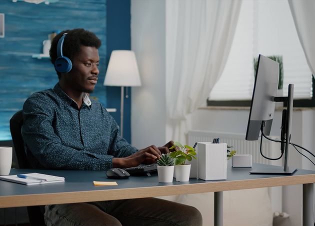 Young Man Using Headphones Listen Music while Working from Home Office Computer