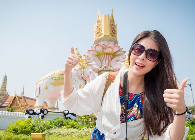Young Beautiful Backpacker Woman Visiting Bangkok Thailand Taking Picture with Famous Awesome Grand Palace Showing Thumb up Gesture Happily Face Camera