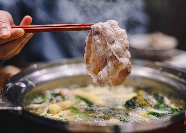 Hand Holding Chopsticks with Ripe Kurobuta Pork Shabu Shabu Sukiyaki Hot Pot Food Concept with Gourmet Japanese Hot Pot Cuisine