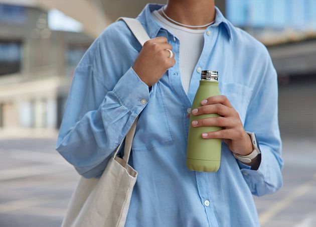 Cropped Shot Unknown Faceless Woman Wears Blue Shirt Carries Fabric Bag Holds Bottle with Fresh Water Strolls Street against Blurred Background Feels Thi