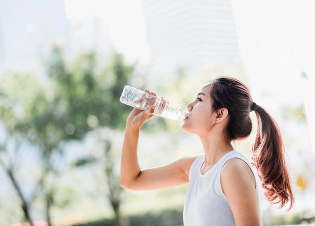 Young Asian Woman Drinking Water from Water Bottle after Jogging Park