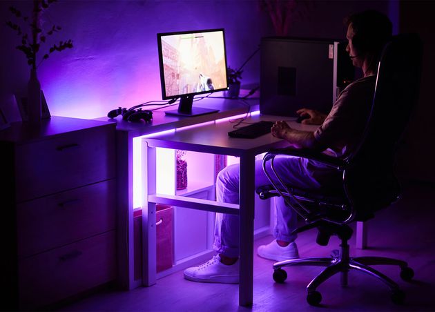 Gamer sitzt am Tisch vor Computermonitor und spielt Computerspiel Dunkler Raum Zuhause