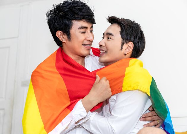 Portrait Asian Homosexual Couple Hug Holding Hand with Pride Flag Bedroom