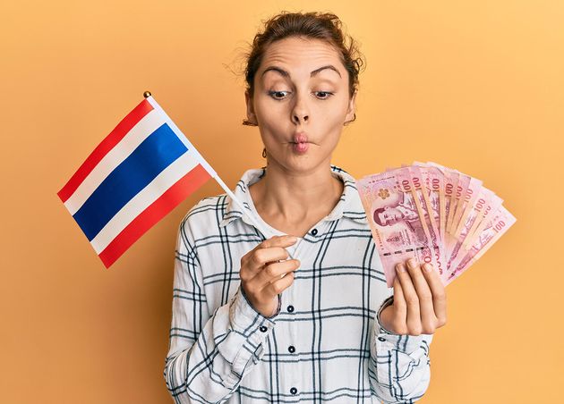 Young Brunette Woman Holding Thailand Flag Baht Banknotes Making Fish Face with Mouth Squinting Eyes Crazy Comical