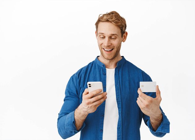 Happy Caucasian Man Looking Smartphone while Paying Online with Credit Card Making Order Mobile App Shopping Internet with Bank Card Cellphone Standing White Wall