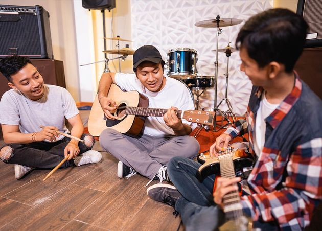 Three Young Asian People Playing Guitar Together while Sitting Floor