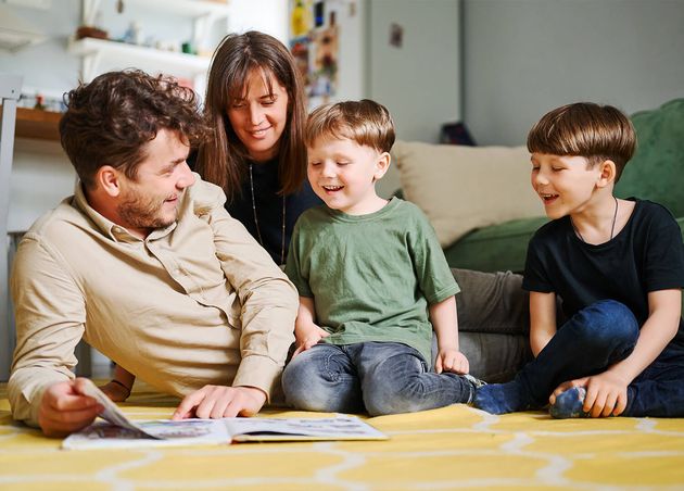 Happy Family with Two Little Sons Reading Story Indoors Parents with Children Spending Time Together Lying Floor Home