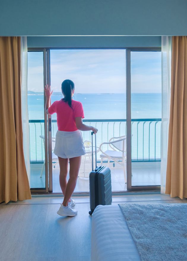 Women with Hand Luggage Trolley Checking Hotel Room Looking out Ocean Thailand