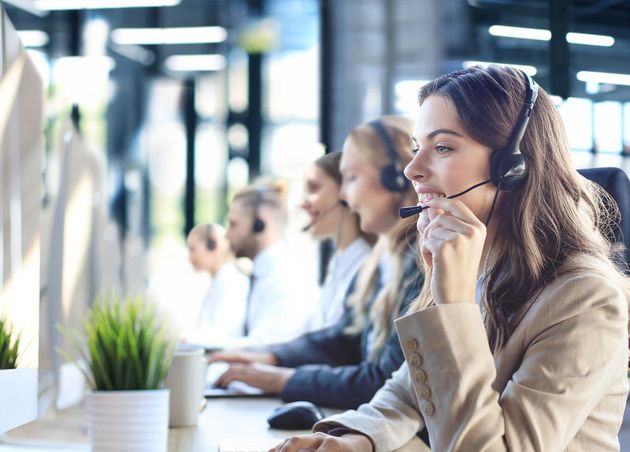 Female Customer Support Operator with Headset Smiling with Collegues Background