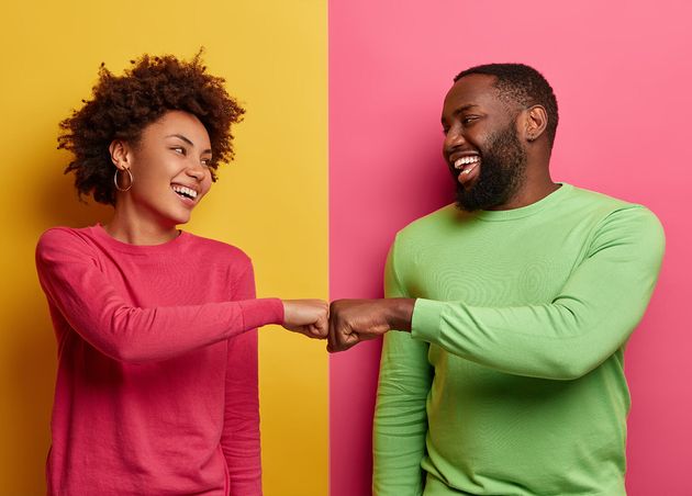 Positive Dark Skinned Young Woman Man Bump Fists Agree Be One Team Look Happily Each Other Celebrates Completed Task Wear Pink Green Clothes Pose Indoor Have Successful Deal